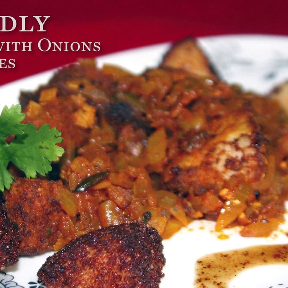Plate of fried idly with onions, tomatoes, browned vegetables, cilantro garnish, and sauce.