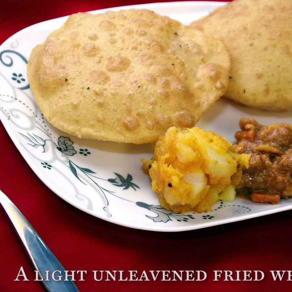 Plate of puffy poori fried wheat breads served with potato curry and vegetable curry on a red tablecloth.