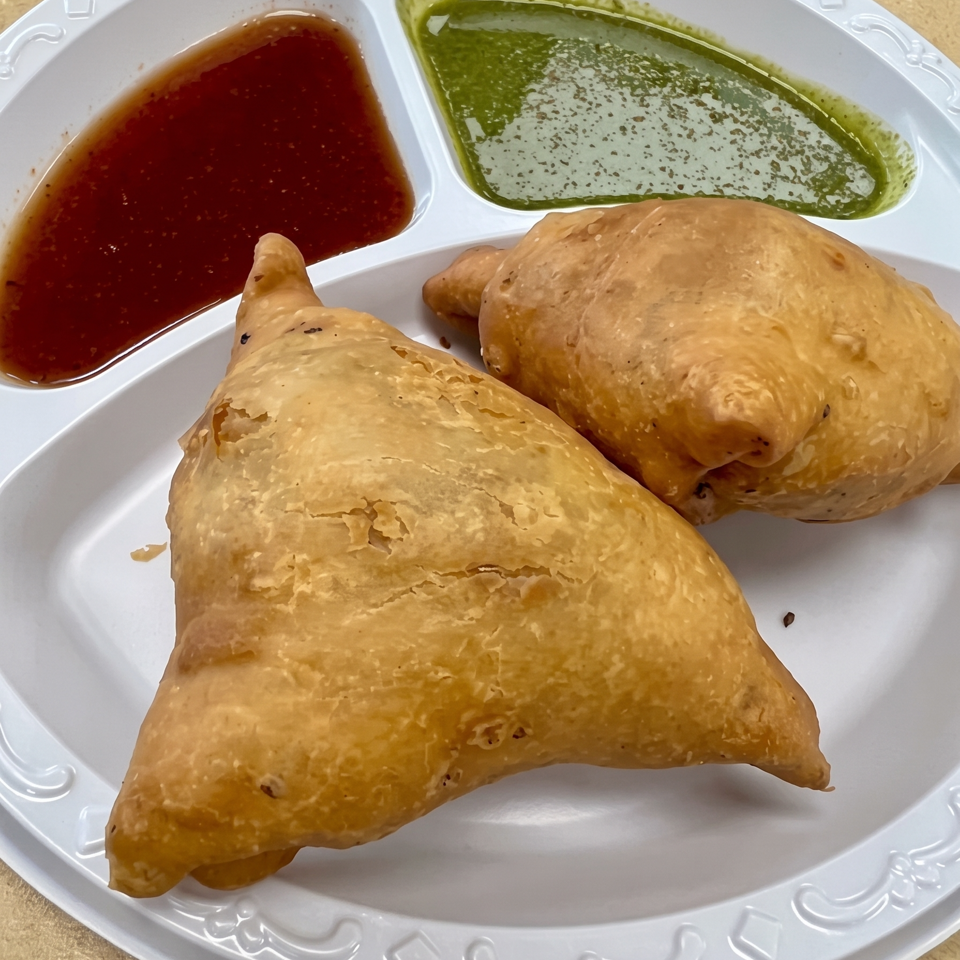 Three golden fried pastries served with red and green dipping sauces on a decorative white plate.